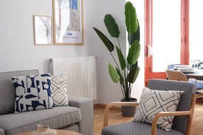 A living room with a grey sofa, a wooden chair, a large green plant, and a radiator.