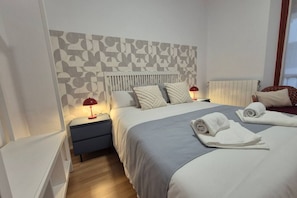 A hotel room with a bed, two bedside tables, a red lamp, a radiator, and a window.