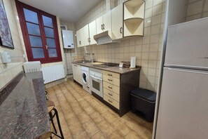 Eine Küche mit Waschmaschine, Kühlschrank und einem Fenster mit rotem Rahmen.