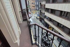 Ein Balkon mit Metallgeländer, der auf eine Straße mit Gebäuden blickt.