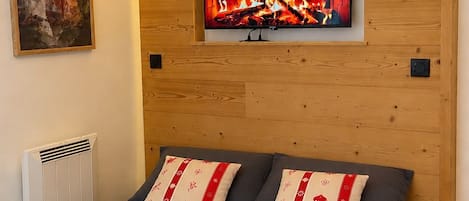 A bedroom with a bed, pillows, a painting, and a TV screen displaying a fireplace.