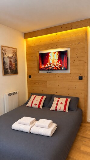 Une chambre à coucher avec un lit, des oreillers, un tableau et un écran de télévision qui affiche une cheminée.