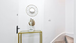 En hall med en vit dörr, ett glasbord med guldfärgad ram, en dekorativ spegel och en väggmonterad ljusströmbrytare.
