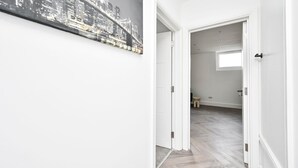 En hall med en målning som föreställer en stadsbild, en dörr som leder till ett rum med ett fiskbensmönstrat golv och en liten pall.