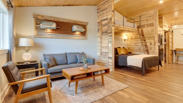 Een gezellige kamer met een bank, een houten salontafel, een bed en een ladder naar een hoger niveau.