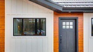 Een modern gebouw met een groot raam en een donkere deur, met een witte buitenkant en houten details.