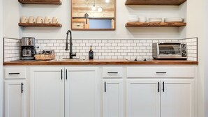Een keuken met witte kastjes, een houten aanrecht, een koffiezetapparaat, een broodrooster en planken met mokken en servies.