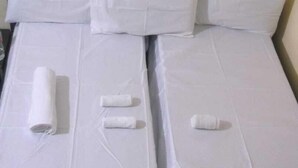 A bed with white linens, including a rolled towel and two pillows. - ANNAPURNA GUEST HOUSE (Nagpur)