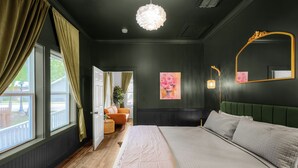 Ein Schlafzimmer mit einem großen Bett, einem grünen Kopfteil, einem Spiegel und einem Bild an der Wand.