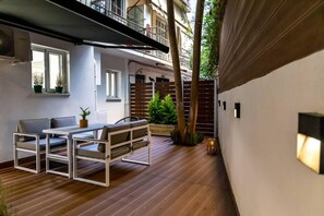 A modern outdoor seating area with a wooden table and chairs, surrounded by potted plants and a wooden fence.