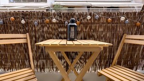 A wooden table with a lantern on top, surrounded by two wooden chairs, set against a bamboo fence with string lights. - Historical Center Athens Amazing Studio (Athens)