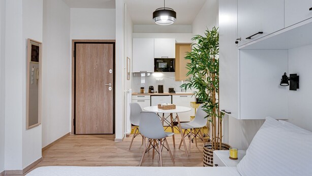 A modern, compact living space with a wooden door, a dining area with a round table and chairs, a kitchen with white cabinets, and a bed with white bedding. - Historical Center Athens Amazing Studio (Athens)