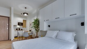 A modern bedroom with a large bed, a small desk, and a chair. There is a plant and a lamp on the desk. - Historical Center Athens Amazing Studio (Athens)