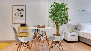 A modern living room with a white sofa, a small round table with chairs, a potted plant, and a framed artwork on the wall. - Historical Center Athens Amazing Studio (Athens)