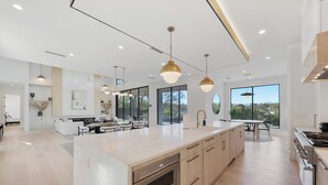 Une cuisine moderne dotée d’un grand îlot central, d’appareils électroménagers en acier inoxydable et de luminaires suspendus.
