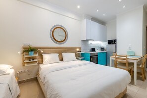 Une chambre avec un grand lit, des tables de chevet, un petit bureau et, au fond, une kitchenette.