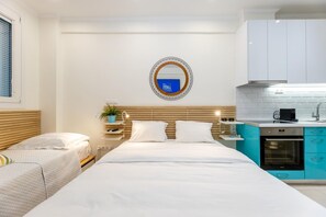 A modern hotel room with a bed, bedside tables, a small kitchen area with a stove, and a mirror on the wall. - Acropolis Museum Amazing Studio (Athens)