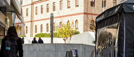 A courtyard with a tiled floor, a black tent, and a building with arched windows in the background.