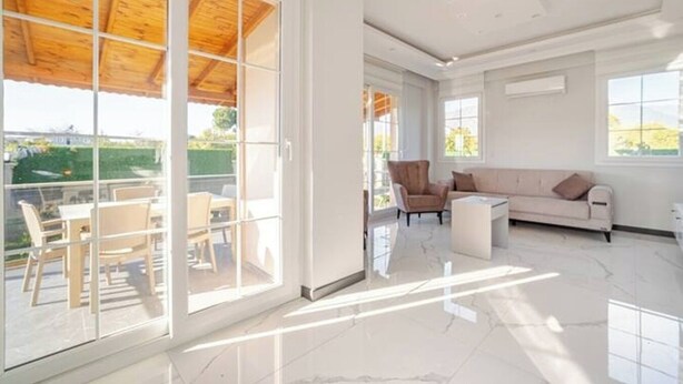Amplia sala de estar con un gran ventanal corredero que da a un patio exterior, un sofá, una silla y una mesa de centro.