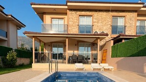 Una casa moderna de dos pisos con piscina, mobiliario exterior y vistas a las montañas.