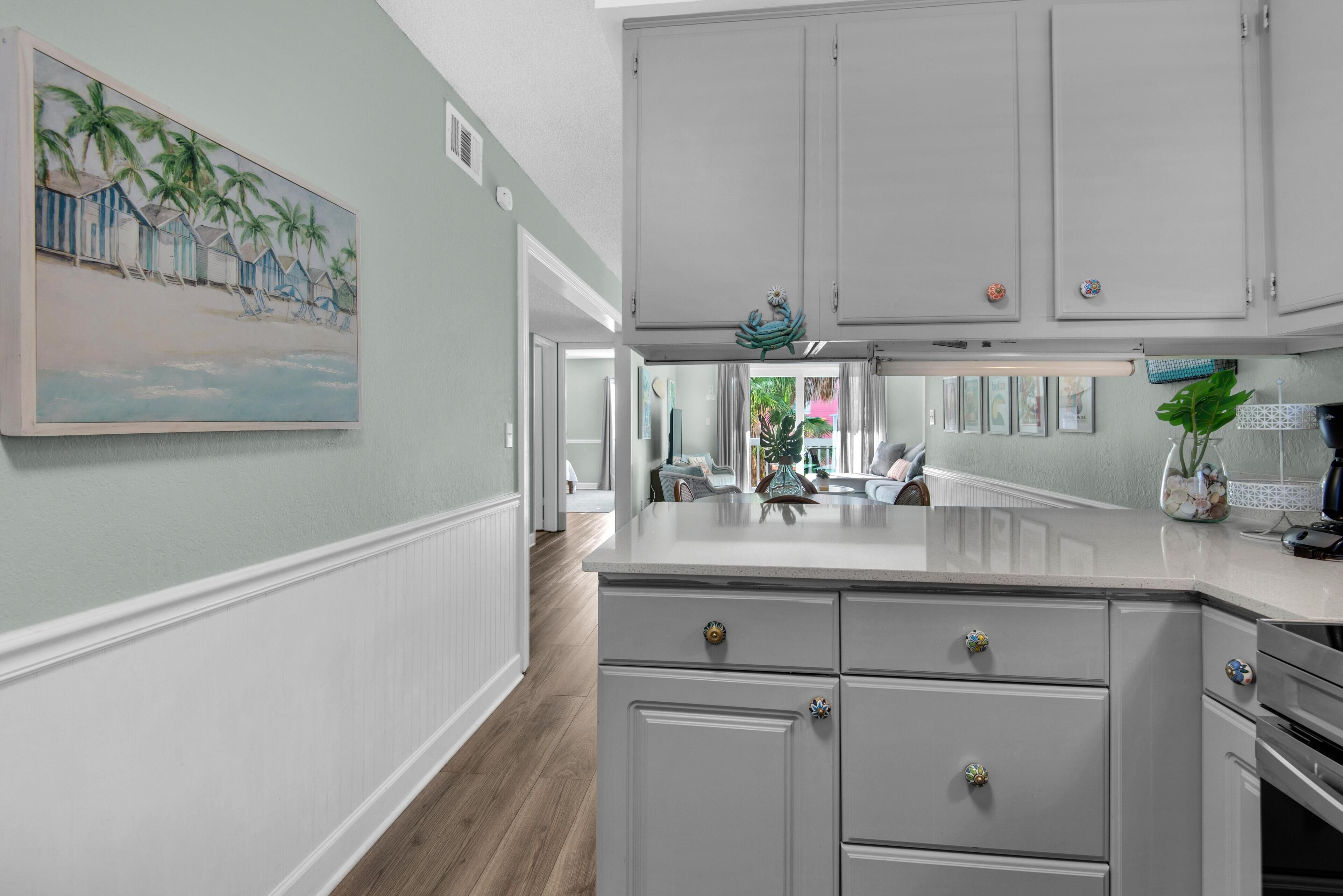A kitchen with white cabinets, a central island, and a painting of a beach scene.