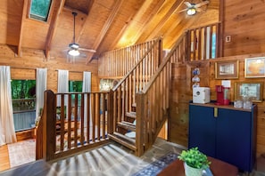 A wooden interior with a staircase, a kitchen area, and a view through a window. - Cozy Cabin Retreat+ Hot Tub + Private + Pet Welcom (Blue Ridge)