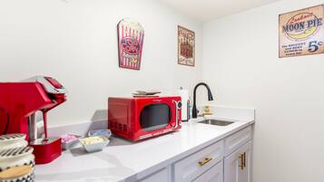 Une cuisine avec un micro-ondes rouge, une machine à café et un évier. On y trouve des décorations murales et un pot de beurre posé sur le comptoir.