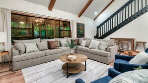 A modern living room with a sectional sofa, a round coffee table, and a staircase.