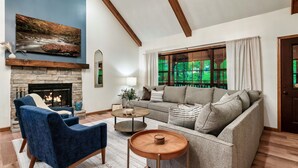 A living room with a fireplace, a sofa, a blue armchair, and a large window with curtains.