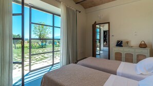 A room with two beds, a large window with curtains, a dresser, and a view of a garden.