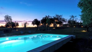 A swimming pool with a clear blue water surface, surrounded by a grassy area with trees and a building in the background.