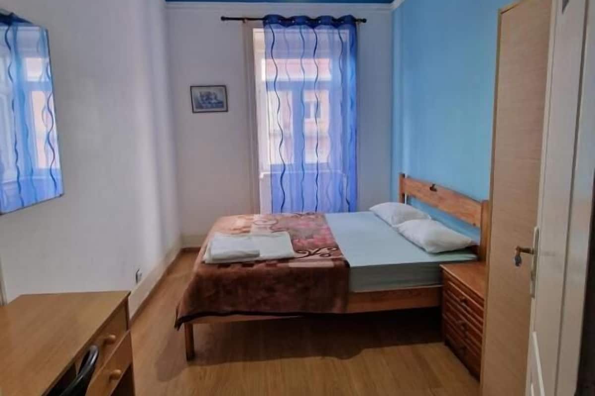 A bedroom with a bed, a desk, a wardrobe, and a window with curtains.