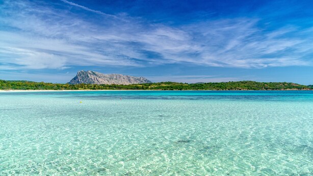 A clear turquoise sea with a rocky mountain in the background.