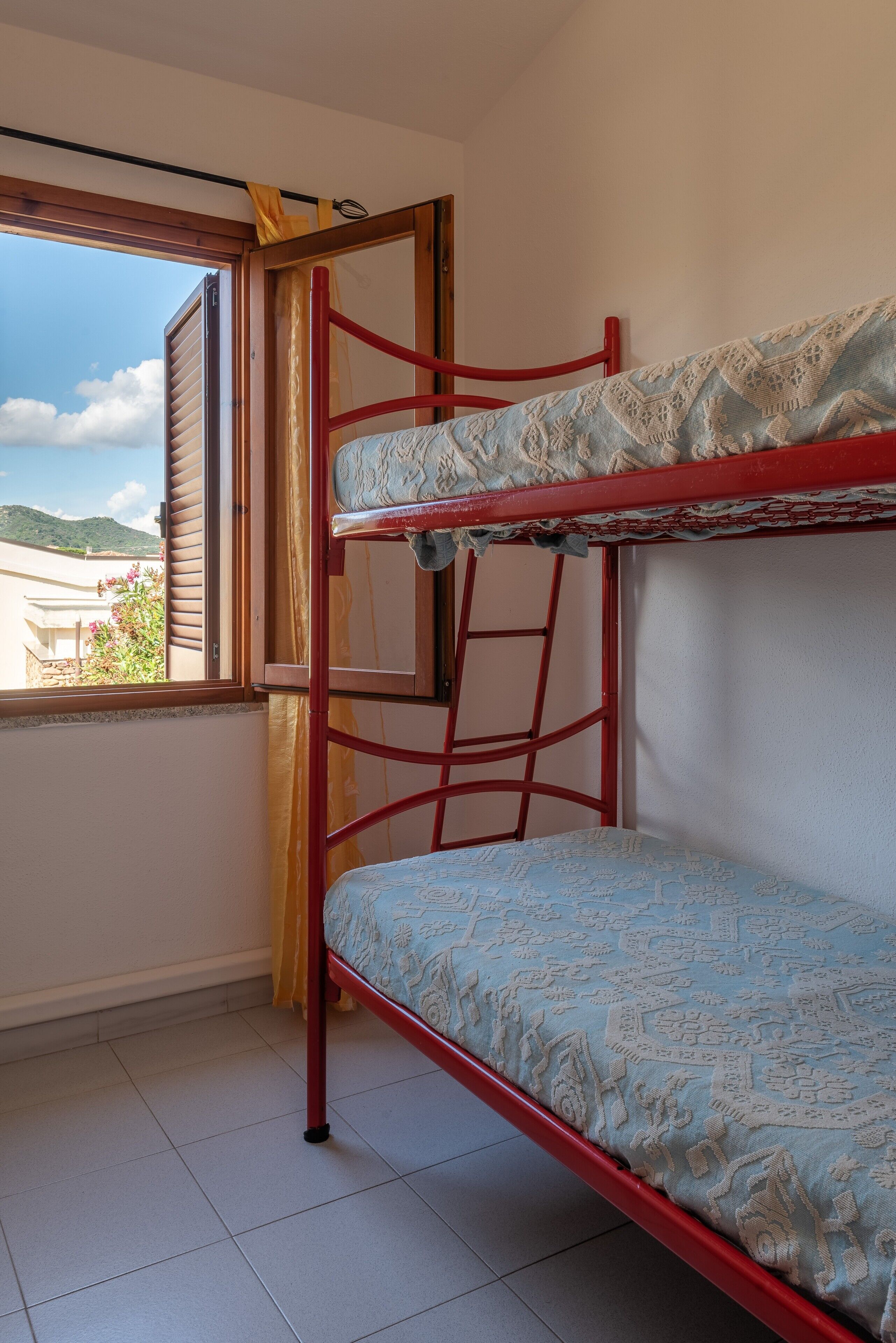 Una cama litera con un colchón estampado, una escalera y una ventana con cortinas.