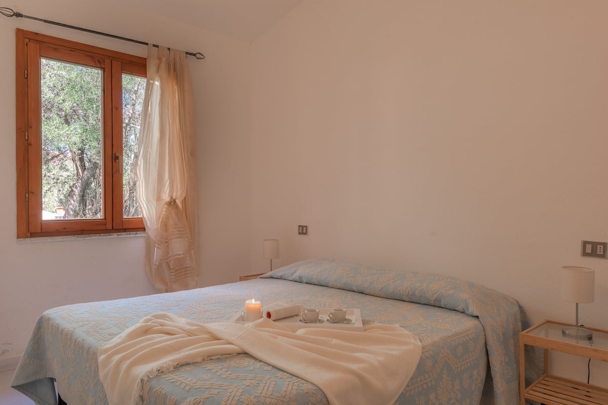 Une chambre à coucher avec un lit, une table de chevet, une lampe et une fenêtre avec des rideaux.