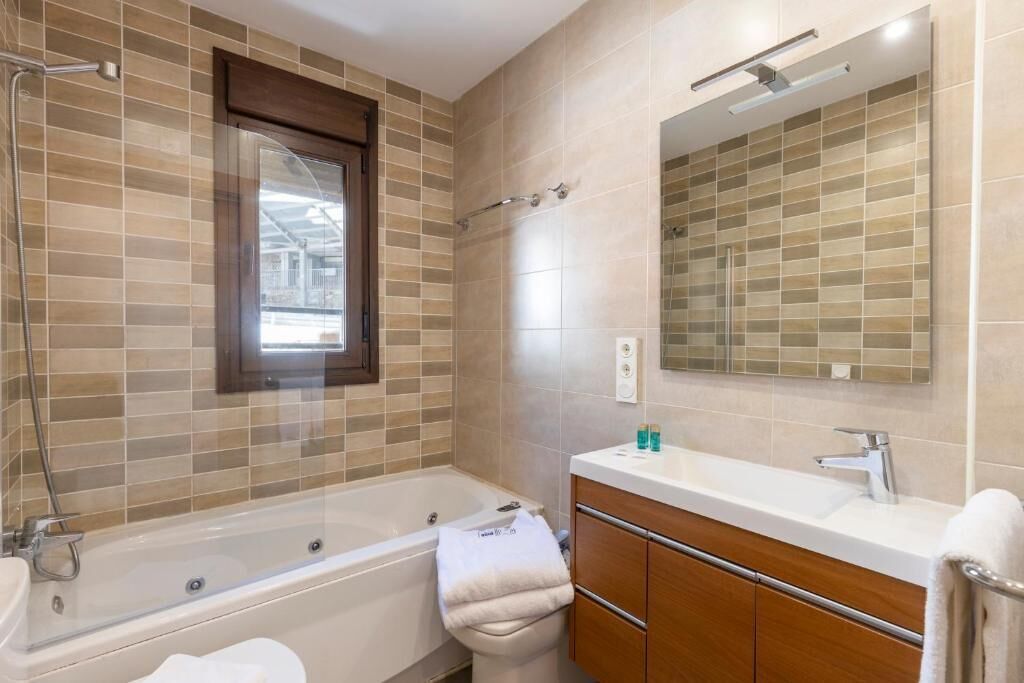 A modern bathroom with a bathtub, a vanity with a mirror, and a window.