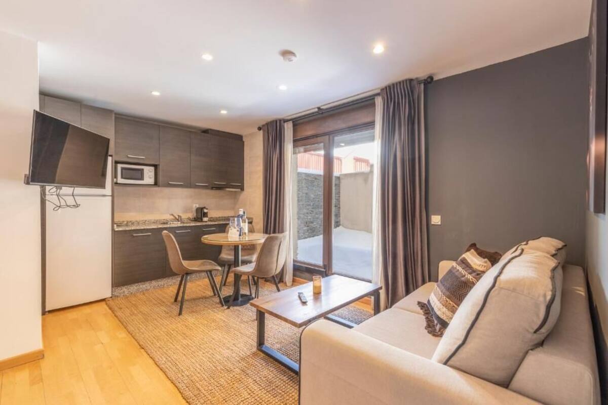 Een ruimtelijk ingerichte leefruimte met kitchenette, een eethoek en een zithoek met een bank en een tafeltje.