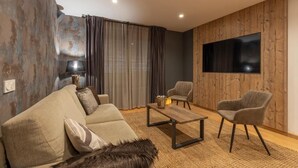 Un salon moderne comprenant un canapé, deux fauteuils, une table basse et un téléviseur à écran plat fixé à un mur en bois.