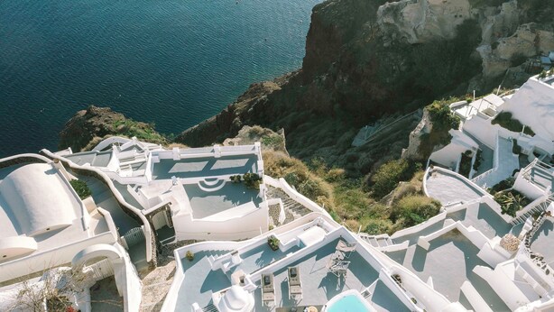 A white-washed coastal building with a swimming pool, outdoor seating, and a view of the sea.