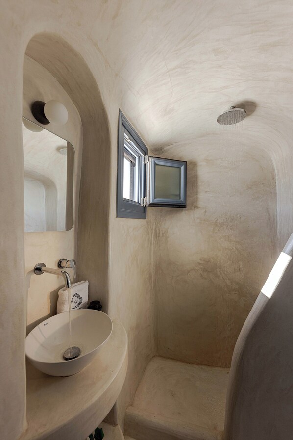 Un baño con lavamanos blanco, espejo y zona de ducha.