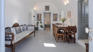 A room with a wooden sofa, a dining table with chairs, a potted plant, and a door with a light switch.