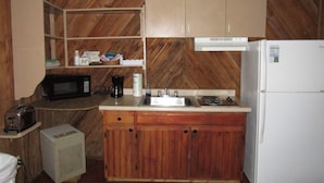A compact kitchen with wooden cabinets, a microwave, a coffee maker, a sink, and a refrigerator. - SpringHouse at Convict Springs (Mayo)