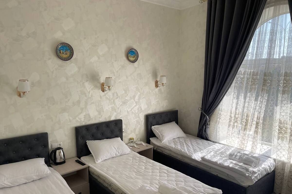 Habitación de hotel con dos camas individuales, una mesita de noche con hervidor y placas decorativas en la pared.