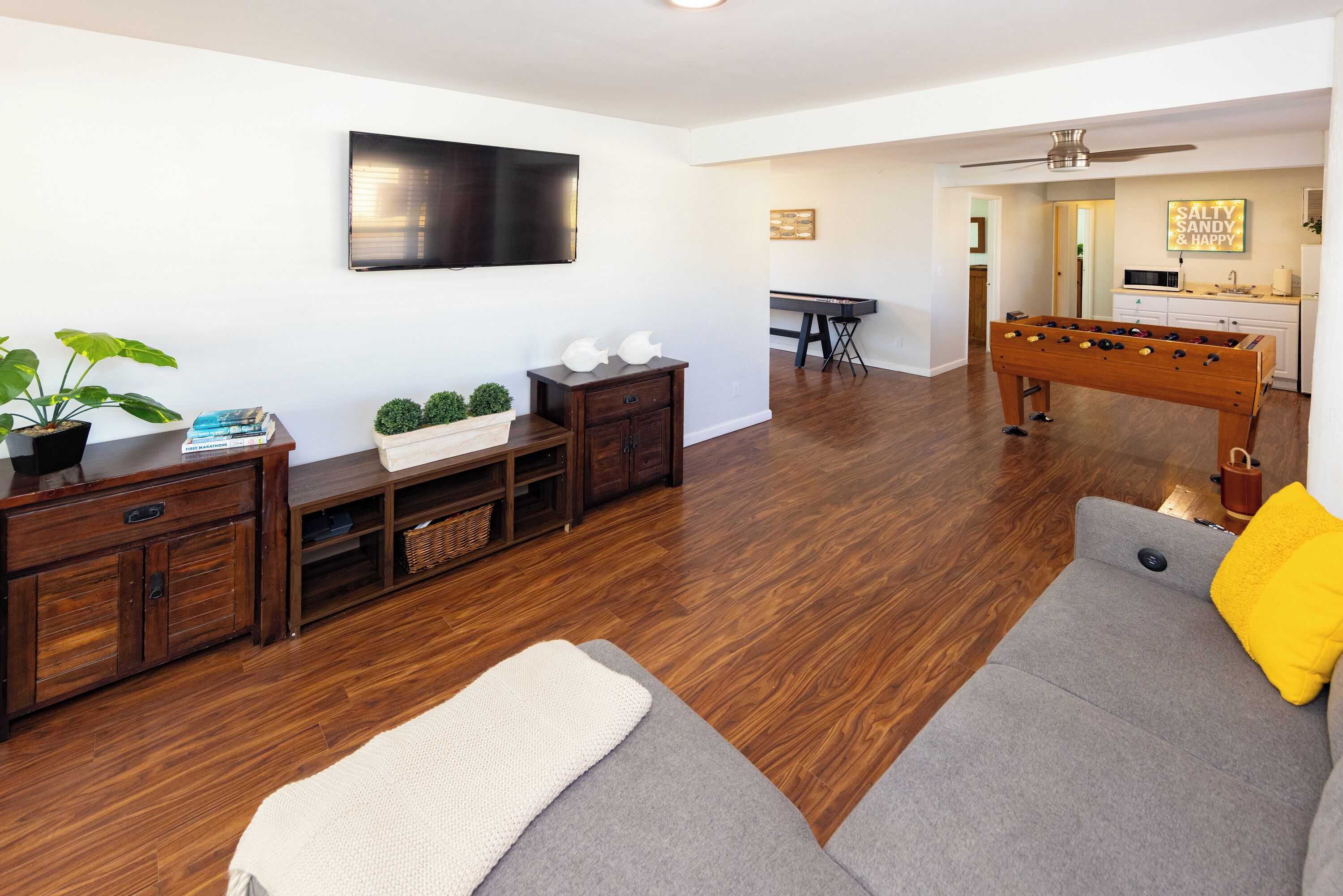 A living room with a gray sofa, wooden entertainment center, flat-screen TV, and a foosball table.