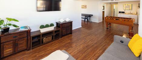 A living room with a gray sofa, wooden entertainment center, flat-screen TV, and a foosball table.