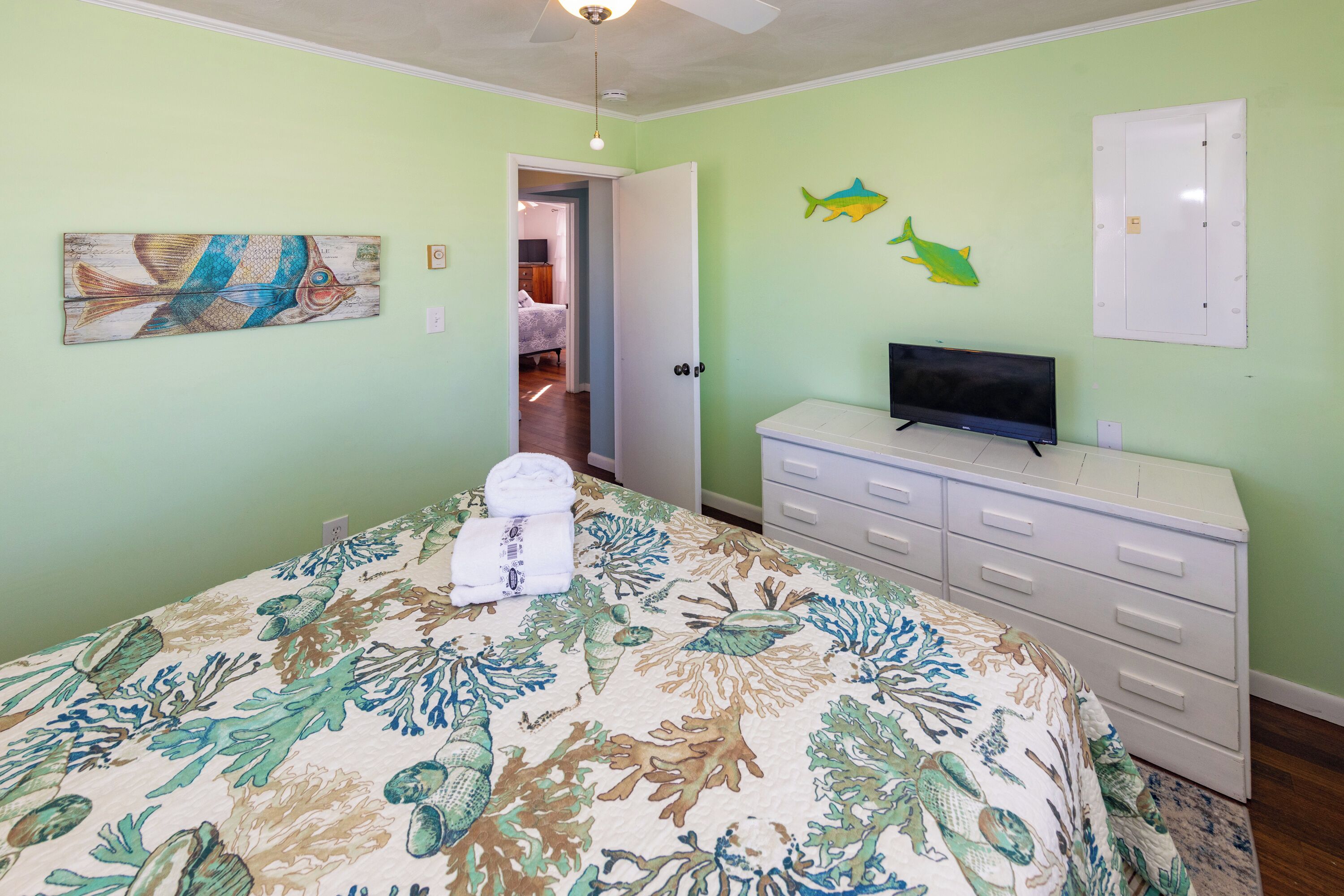 A bedroom with a bed, a dresser, a television, and a door leading to another room.
