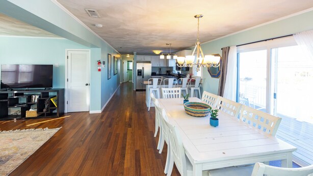 A spacious dining area with a long white table and chairs, a television, and a kitchen in the background.