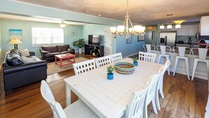 A spacious living room with a white dining table, comfortable seating, and a kitchen area with modern appliances.