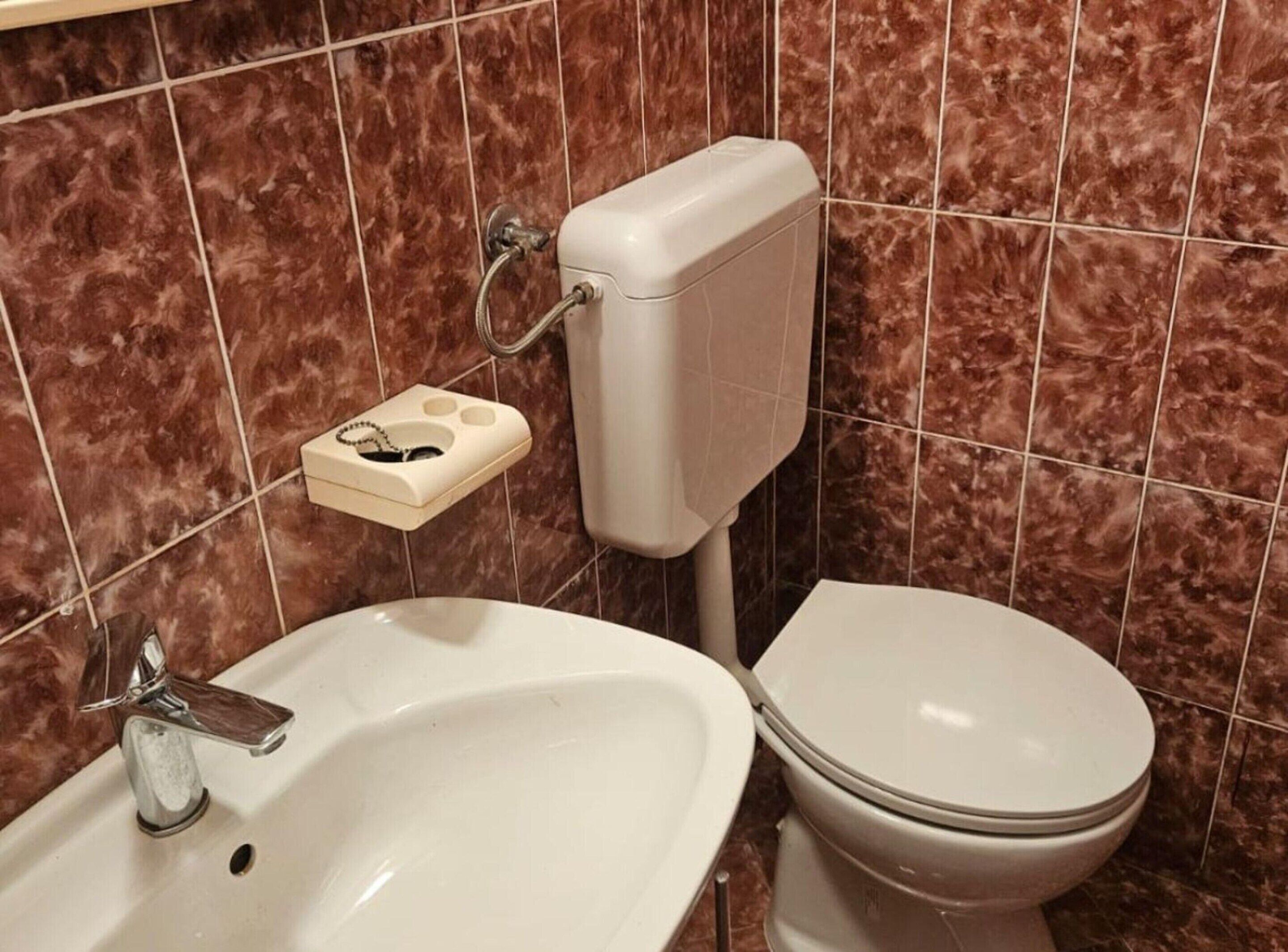 Ein Badezimmer mit einem weißen Waschbecken, einer Toilette und einer Wand mit Marmorfliesen.