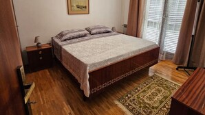 A bedroom with a wooden bed, a nightstand, a lamp, a framed picture on the wall, and a patterned rug. - Apartment in Nature (Kastelir-Labinci)